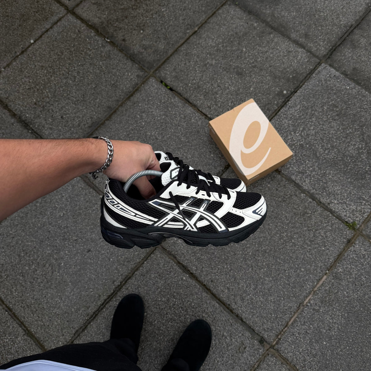 ASICS GEL-1130 Black Cream trainers held in hand showing black mesh upper, cream ASICS stripes and silver detailing