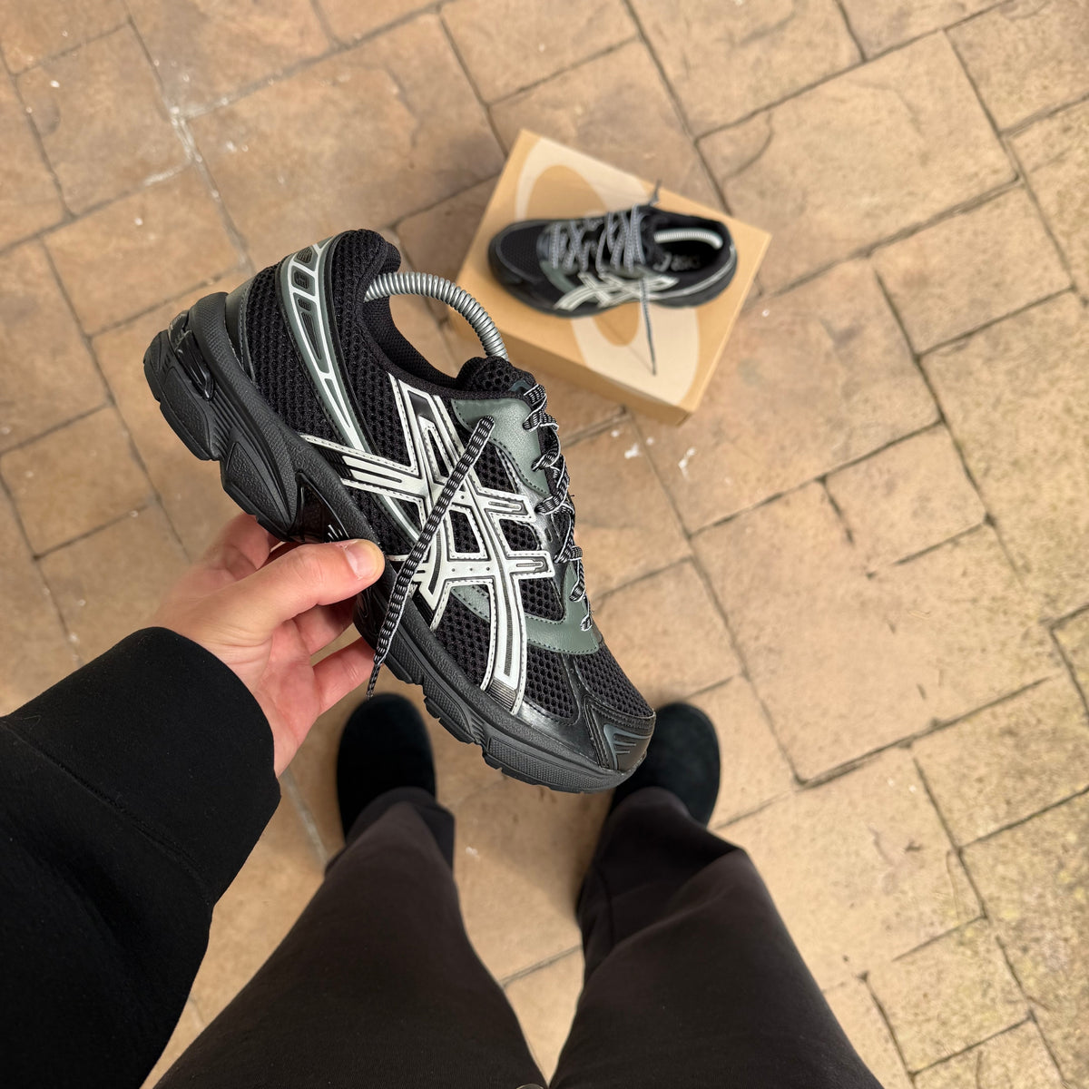 Close-up view of the ASICS Gel-1130 Black Glacier Grey held outdoors highlighting the dark technical upper