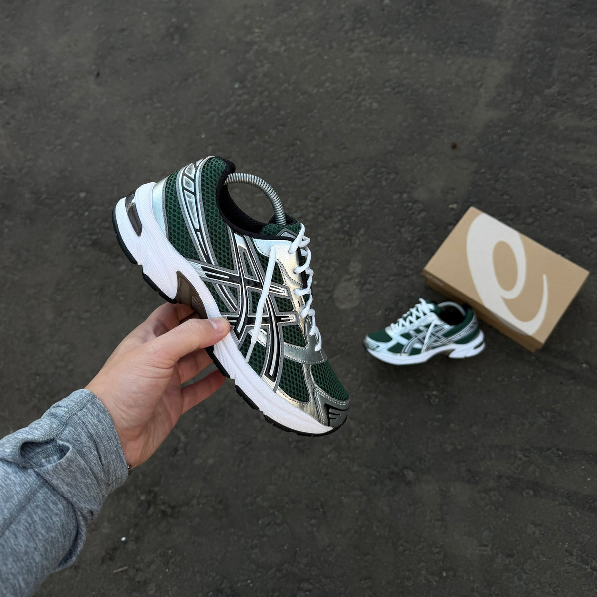 ASICS GEL-1130 Evergreen Black trainers held in hand showing dark green mesh and metallic silver side detailing