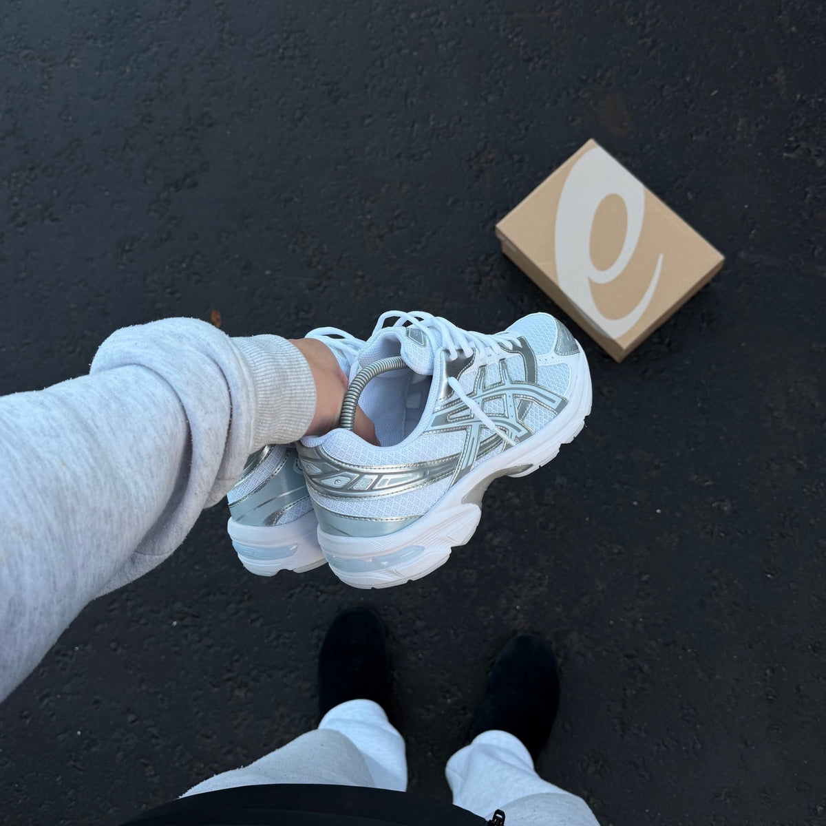 ASICS GEL-1130 White Storm Cloud trainers held above pavement showing white laces and layered upper design