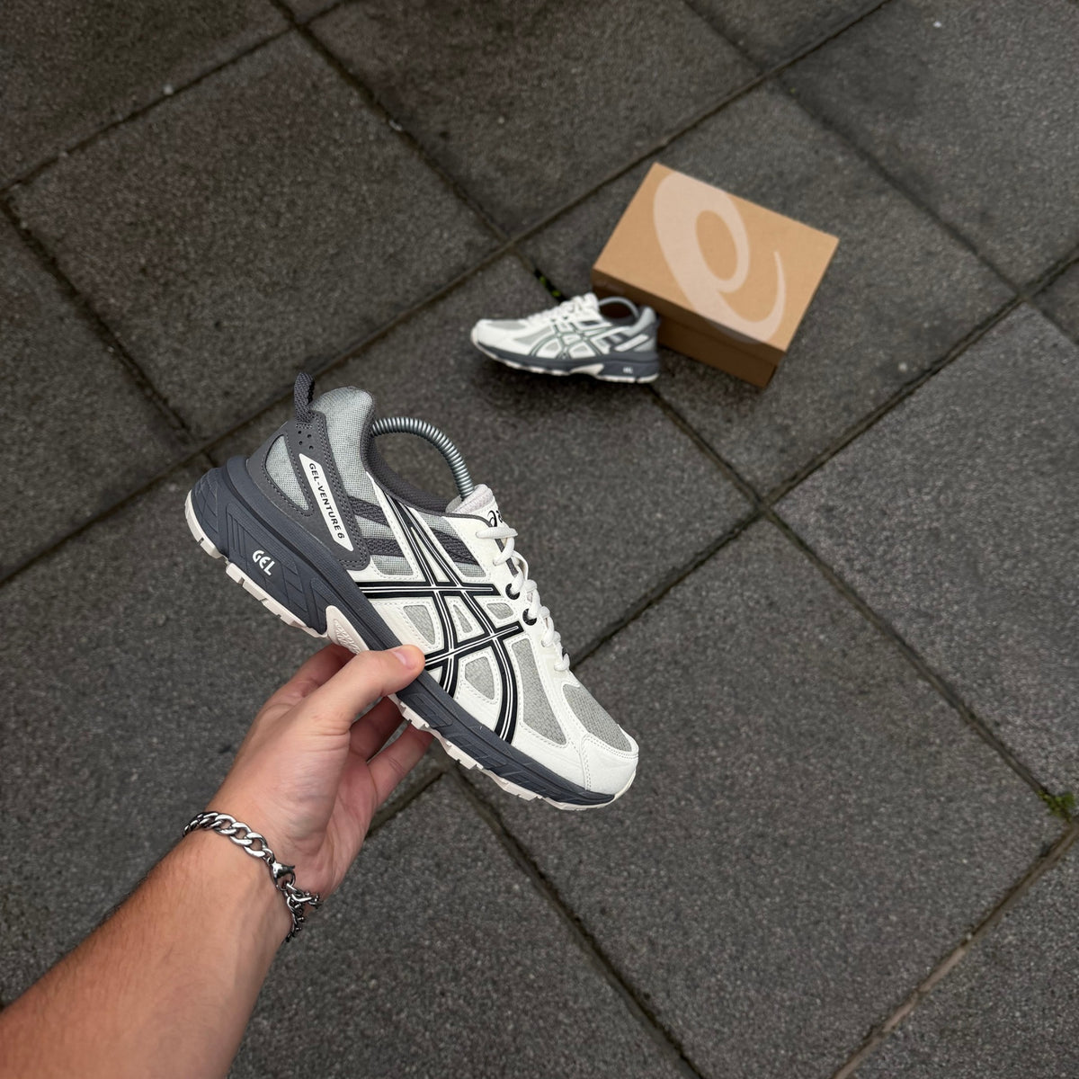 ASICS Gel-Venture 6 Olive Grey Cream trainer held sideways showing layered upper and rugged trail-inspired sole