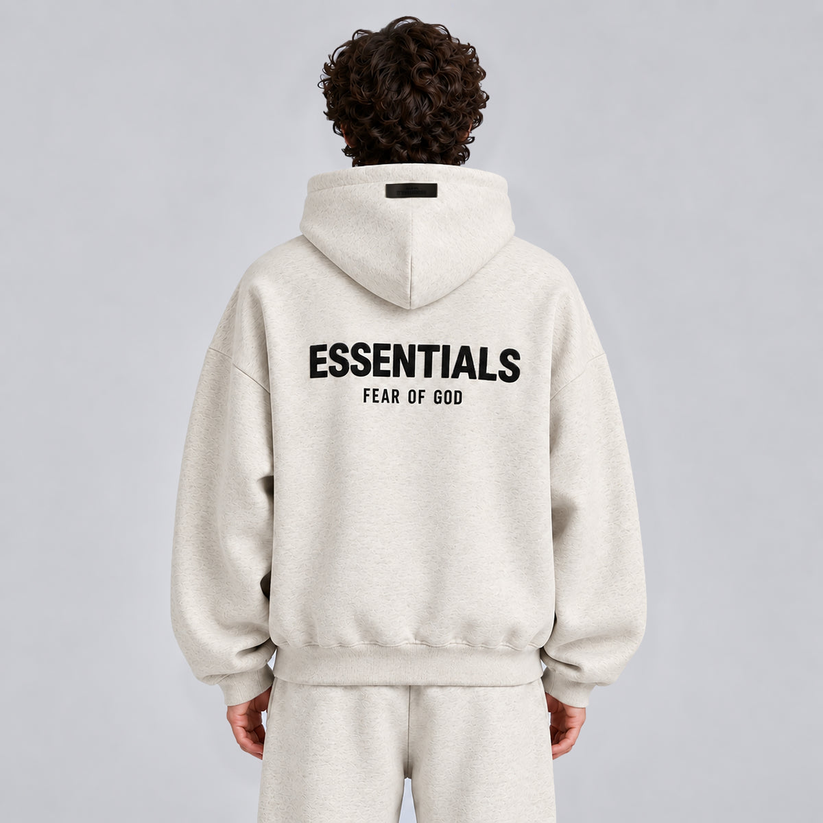 Back view of Fear of God Essentials Light Heather Oatmeal SS22 hoodie showing ESSENTIALS branding