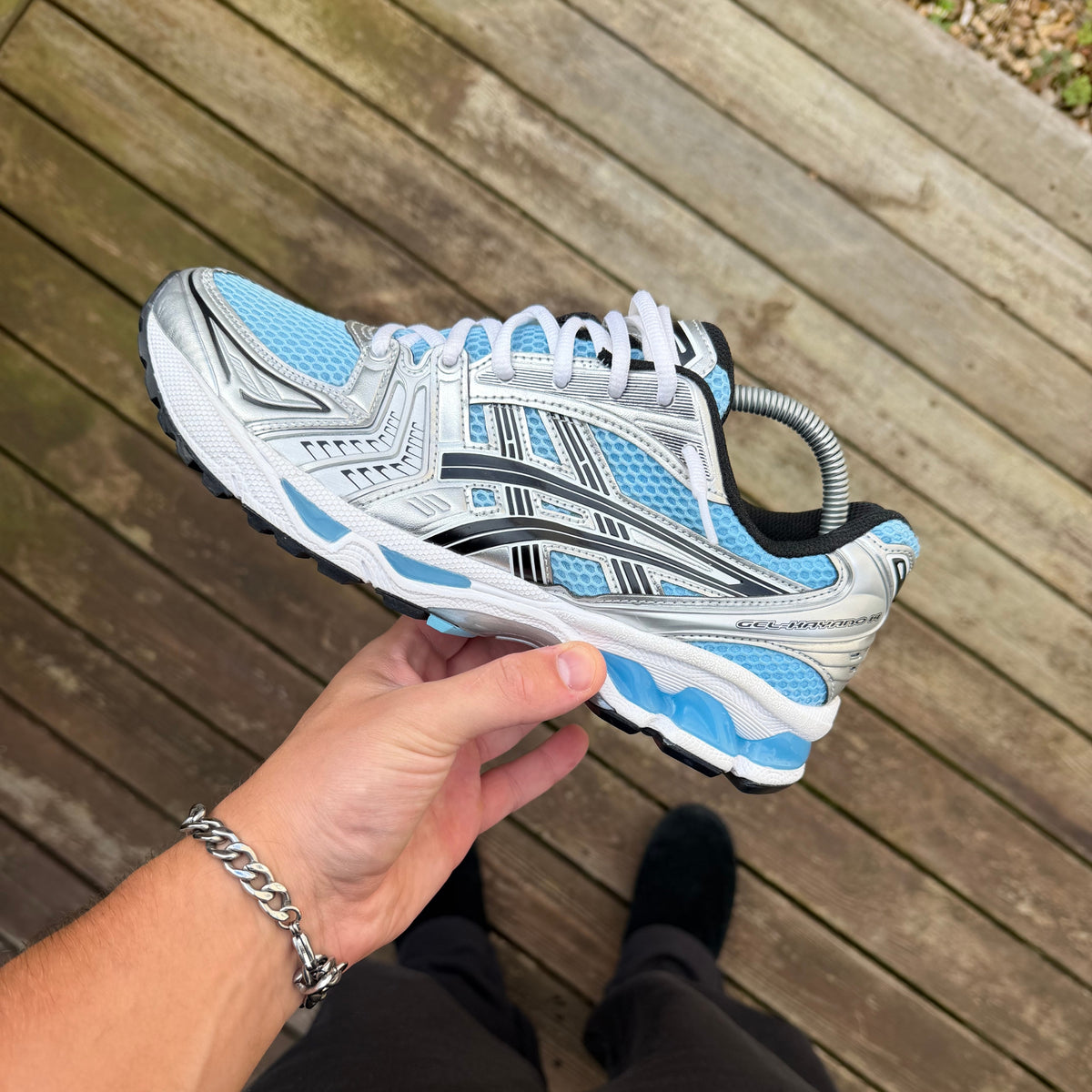 Kayano 14 Arctic Sky trainer held from the side highlighting metallic silver panelling and blue GEL sole details