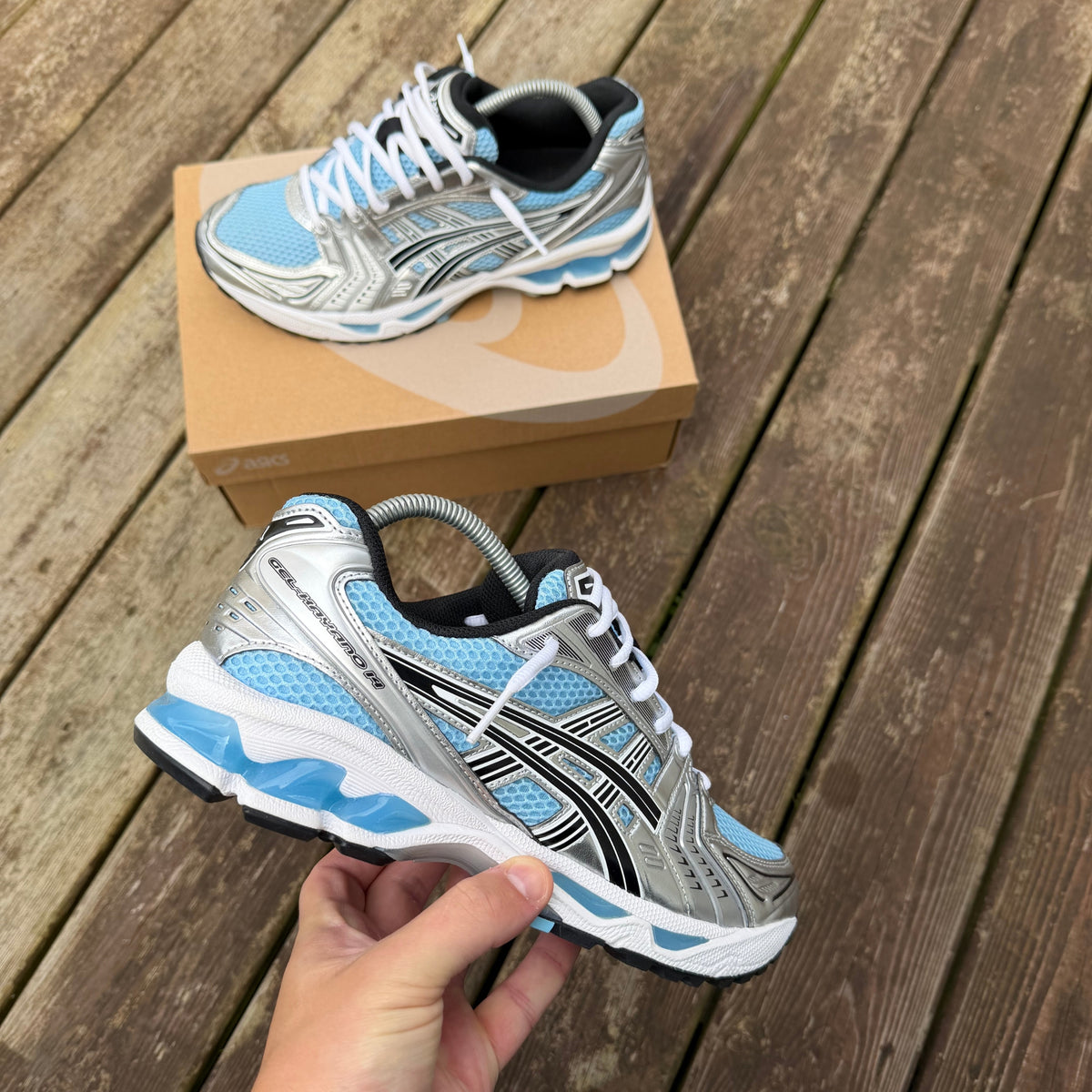 ASICS Arctic Sky Gel-Kayano 14 photographed on wooden decking highlighting the layered blue and silver upper