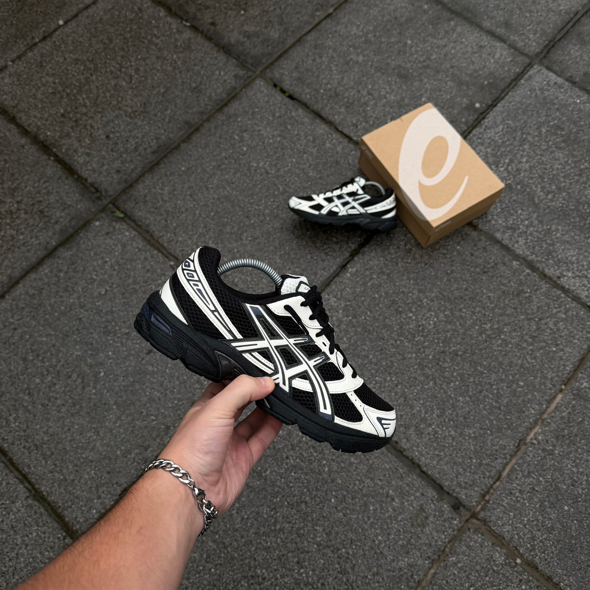 ASICS GEL-1130 Black Cream trainer held at an angle showing retro running silhouette and contrasting cream overlays