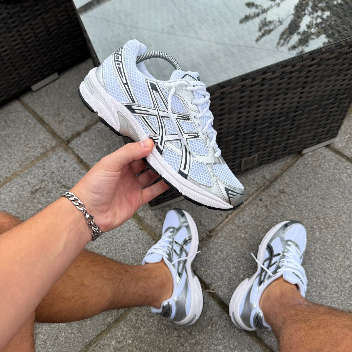 ASICS Gel-1130 White Pure Silver trainer held outdoors showing white mesh and metallic silver overlays