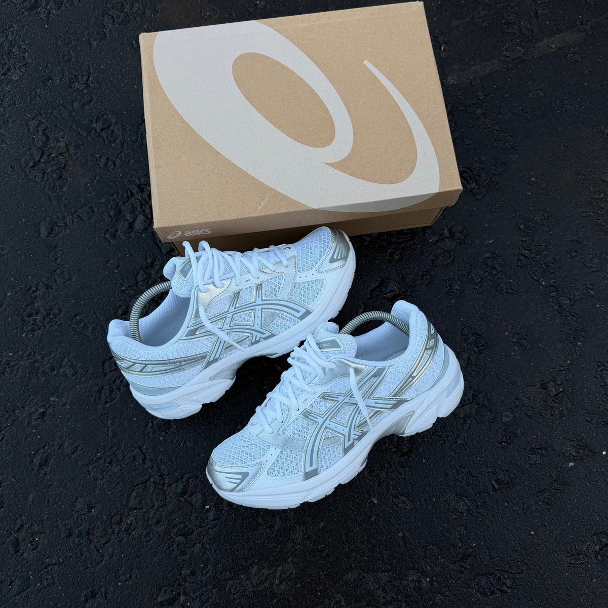 Pair of ASICS GEL-1130 White Storm Cloud trainers displayed on dark pavement showing white mesh and grey overlays