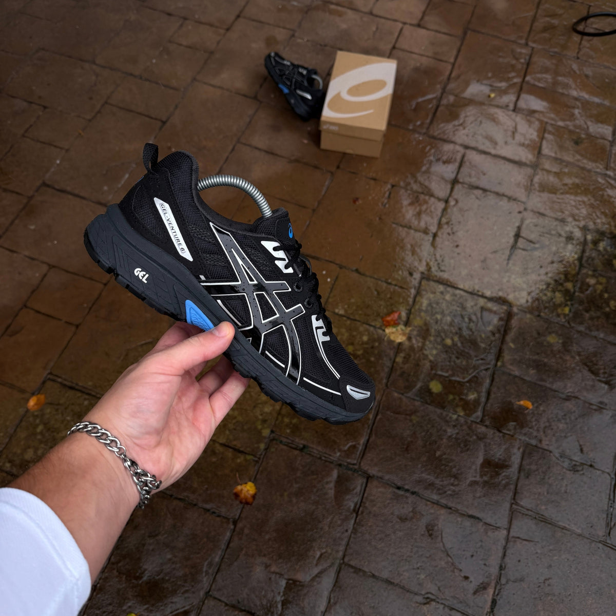 ASICS Gel-Venture 6 Blue Coast black and silver trainer held at an angle outdoors