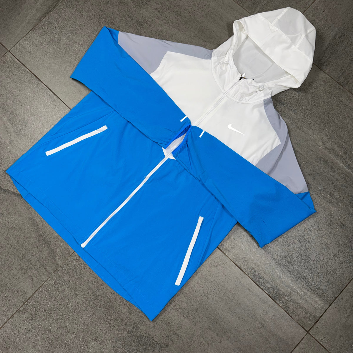 Blue white and grey Nike Windrunner shown flat as part of the Phenom running set