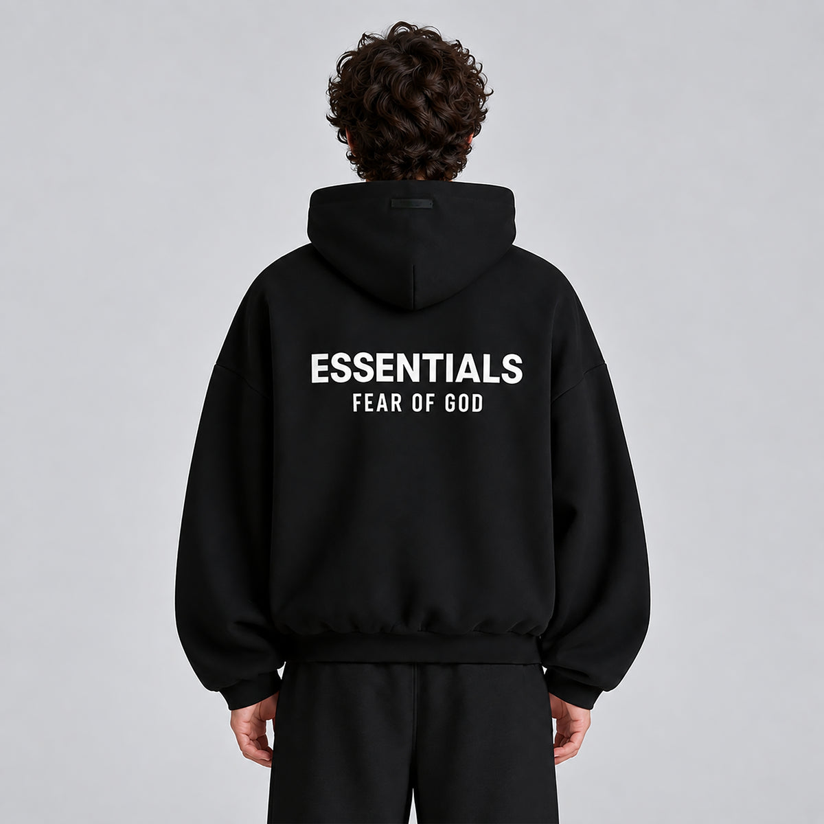 Rear model view of Fear of God Essentials Black Hoodie FW24 showing the large back logo