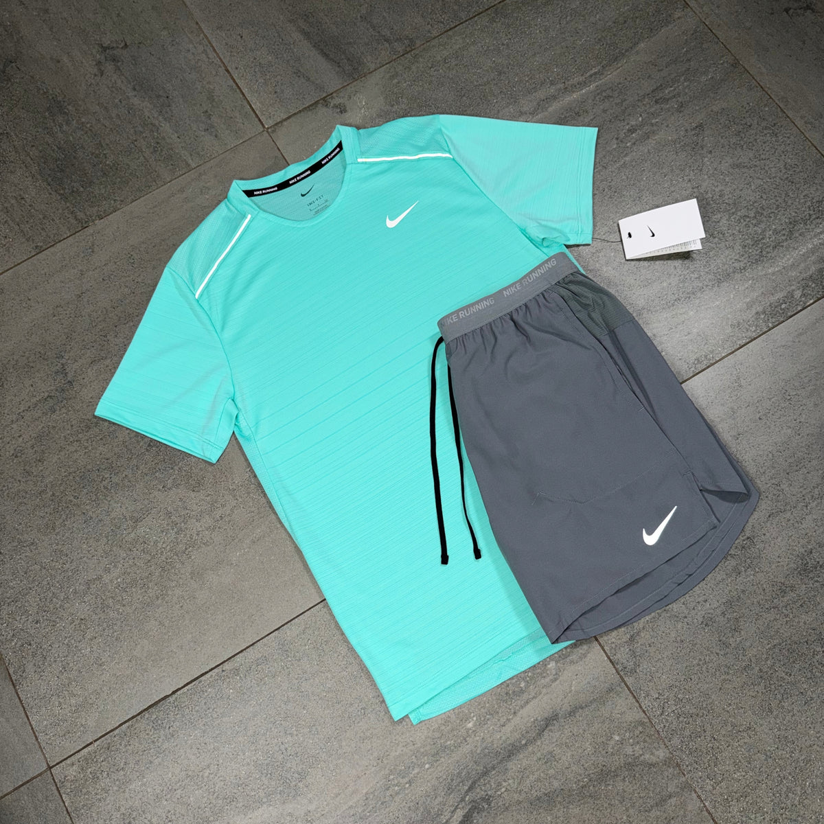 Angled view of a turquoise Nike Miler performance top alongside grey Flex Stride running shorts