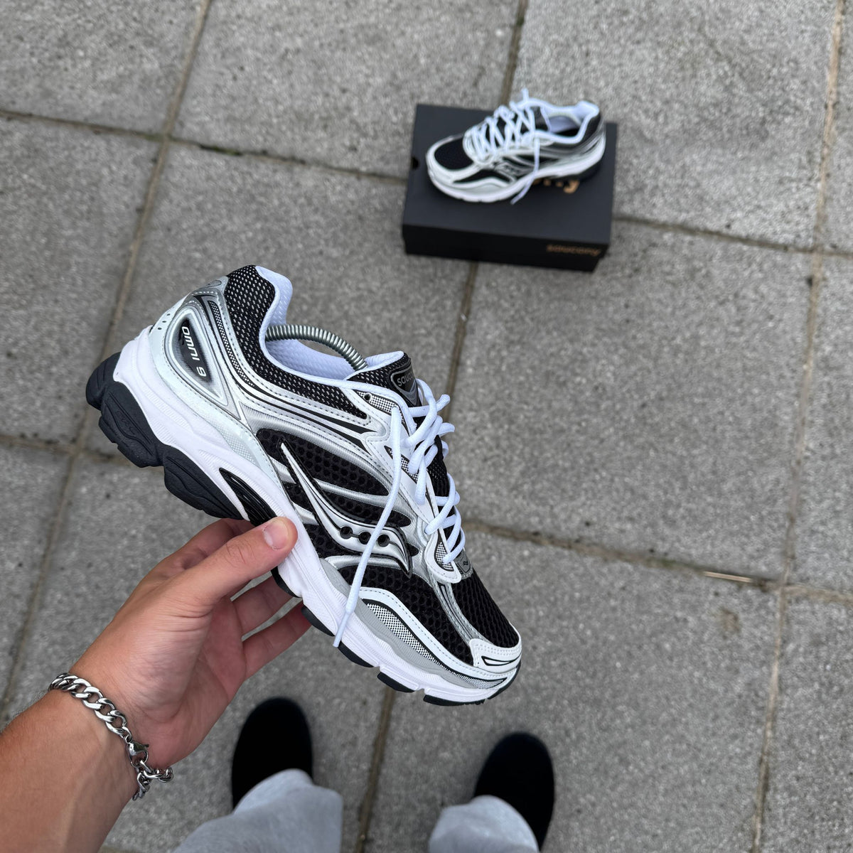 Hand holding Saucony ProGrid Omni 9 Black White trainers showing the layered mesh upper and lacing