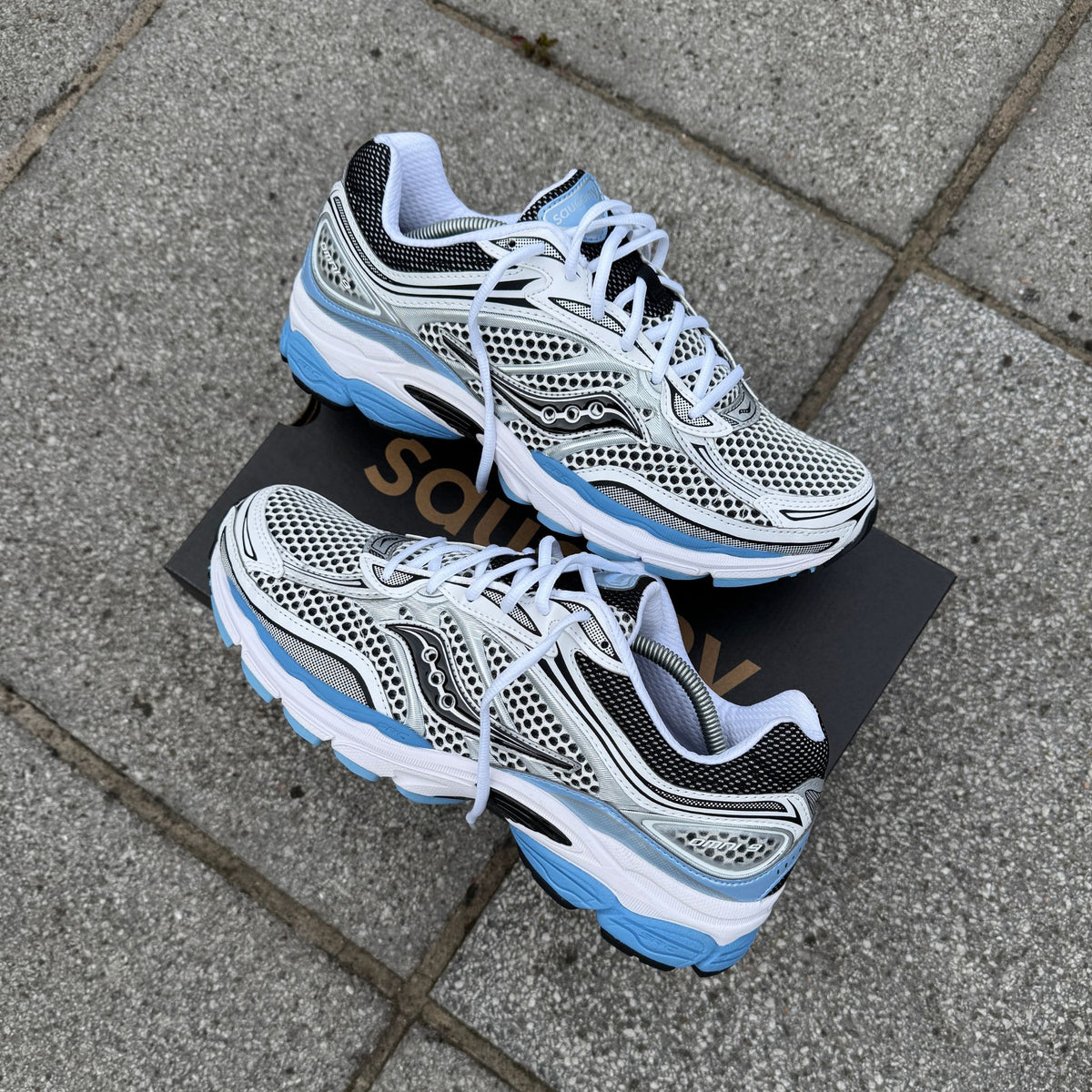 Pair of Saucony ProGrid Omni 9 Blissful Blue trainers arranged on a Saucony box outdoors